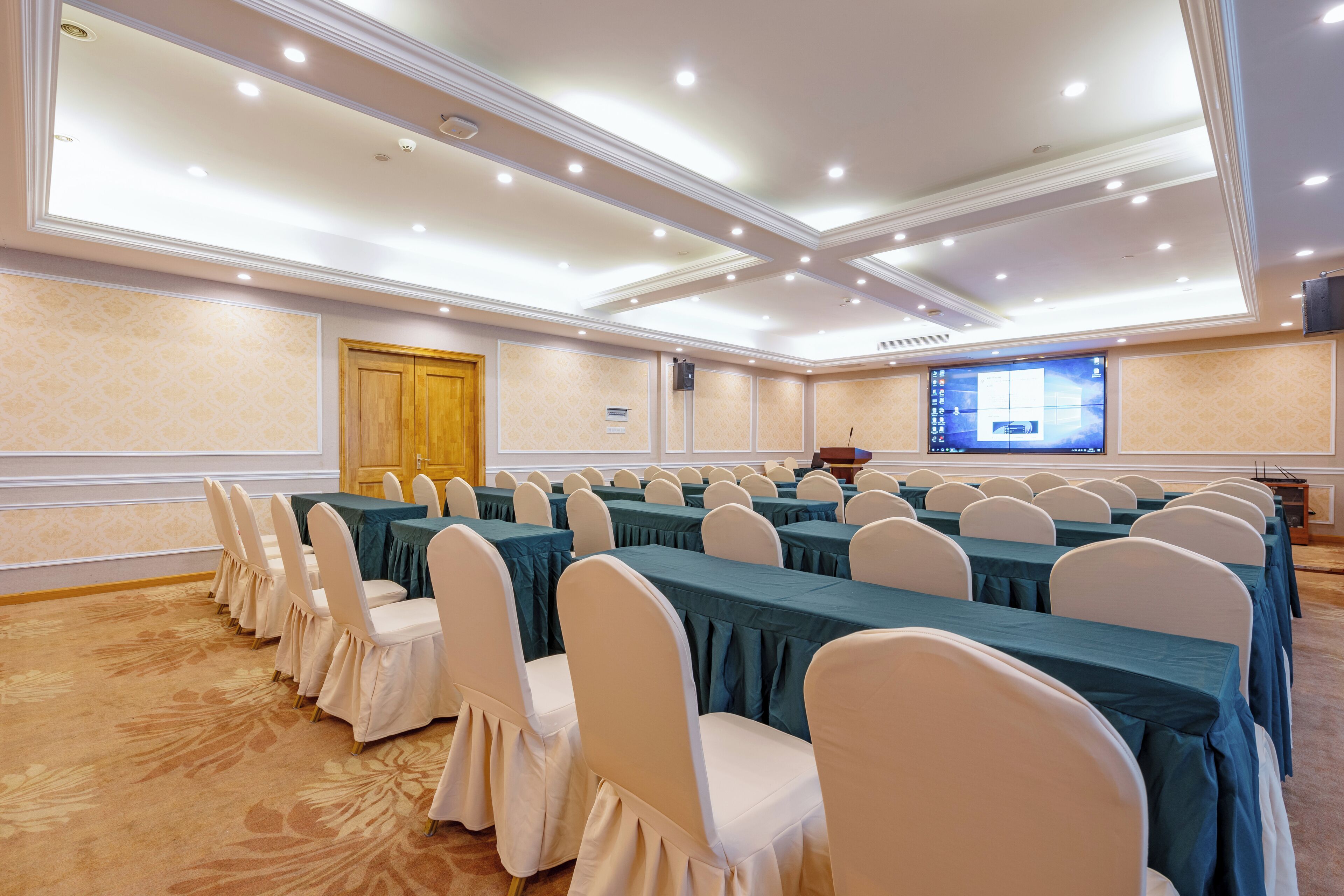 A conference room with rows of tables and chairs, a projector screen, and a wooden door.
