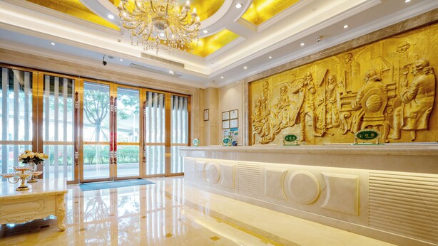 Un lobby lujoso con piso de mármol, un candelabro imponente y un mural grande que representa figuras históricas.