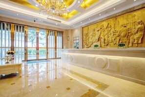 Un lobby lujoso con piso de mármol, un candelabro imponente y un mural grande que representa figuras históricas.