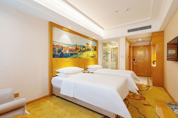 Habitación de hotel con dos camas, un cuadro grande en la pared, una puerta de madera y un separador de vidrio.