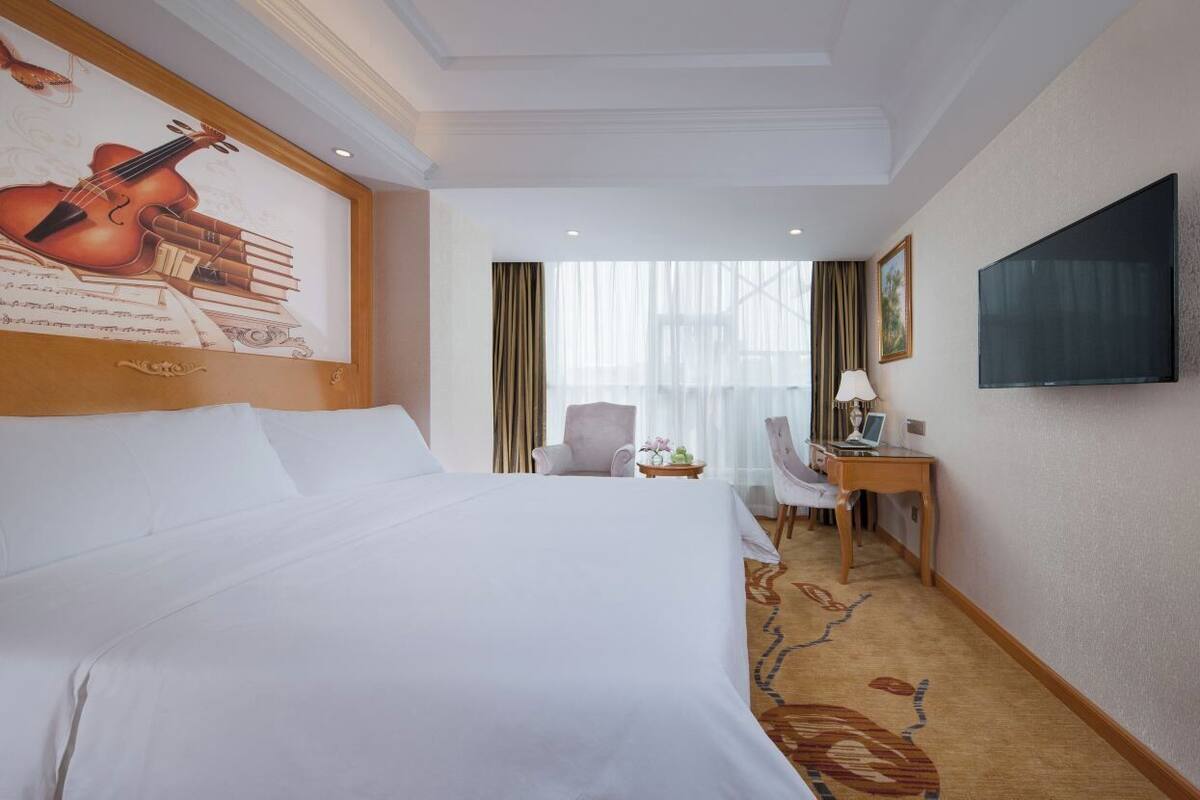 Hotelkamer met een groot bed, een bureau, een stoel, een televisie en een schilderij aan de muur.