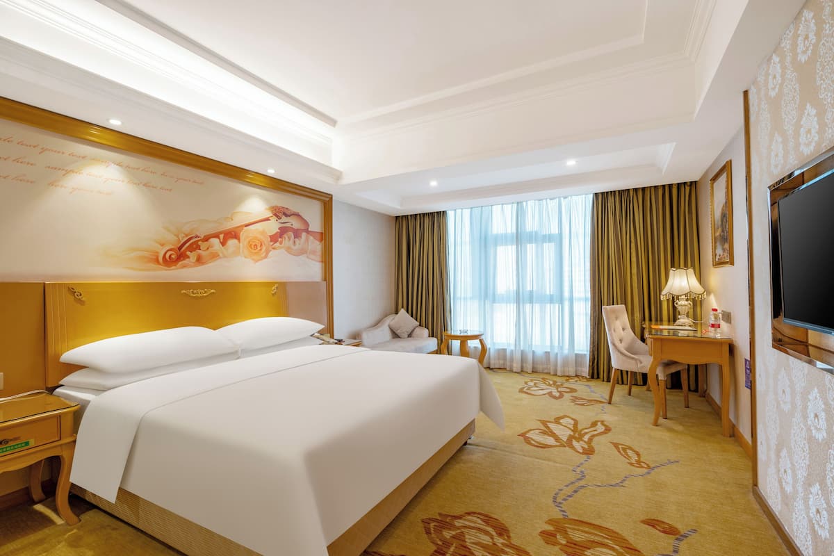 Een hotelkamer met een groot bed, een bureau met lamp, een stoel en een televisie.