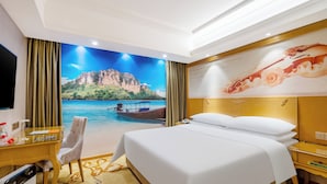 Habitación de hotel con una cama grande, un escritorio con una silla, televisión y un mural de una playa.