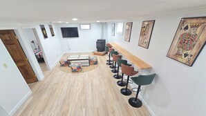 Un interior moderno con suelo de madera, una zona de bar con taburetes, un televisor de pantalla plana y obras enmarcadas en las paredes.