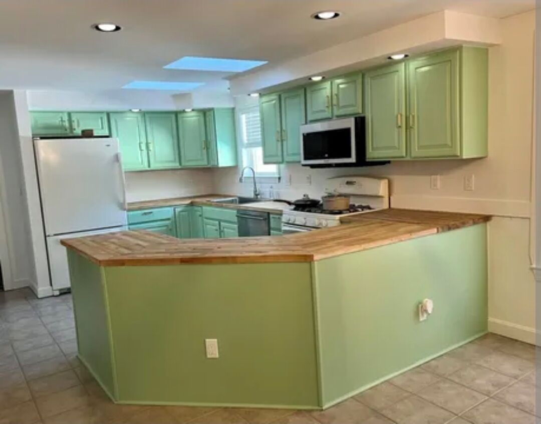 A kitchen with green cabinets, a wooden countertop, and a built-in microwave.