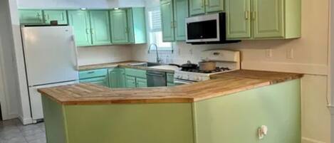 A kitchen with green cabinets, a wooden countertop, and a built-in microwave.