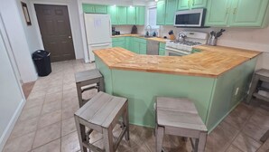 Una cocina con gabinetes verdes, una isla de madera, un refrigerador, un microondas y una estufa.