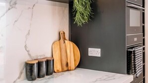 Una cocina moderna con encimera de mármol, armarios oscuros, tabla de cortar de madera y una planta en maceta.