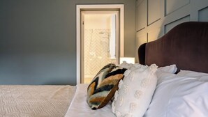 Un dormitorio con cama, un cojín estampado y una puerta que da al baño.