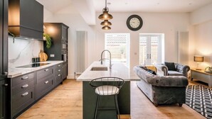 Una cocina moderna con una isla central, muebles oscuros y un área de comedor con sofá y lámpara.