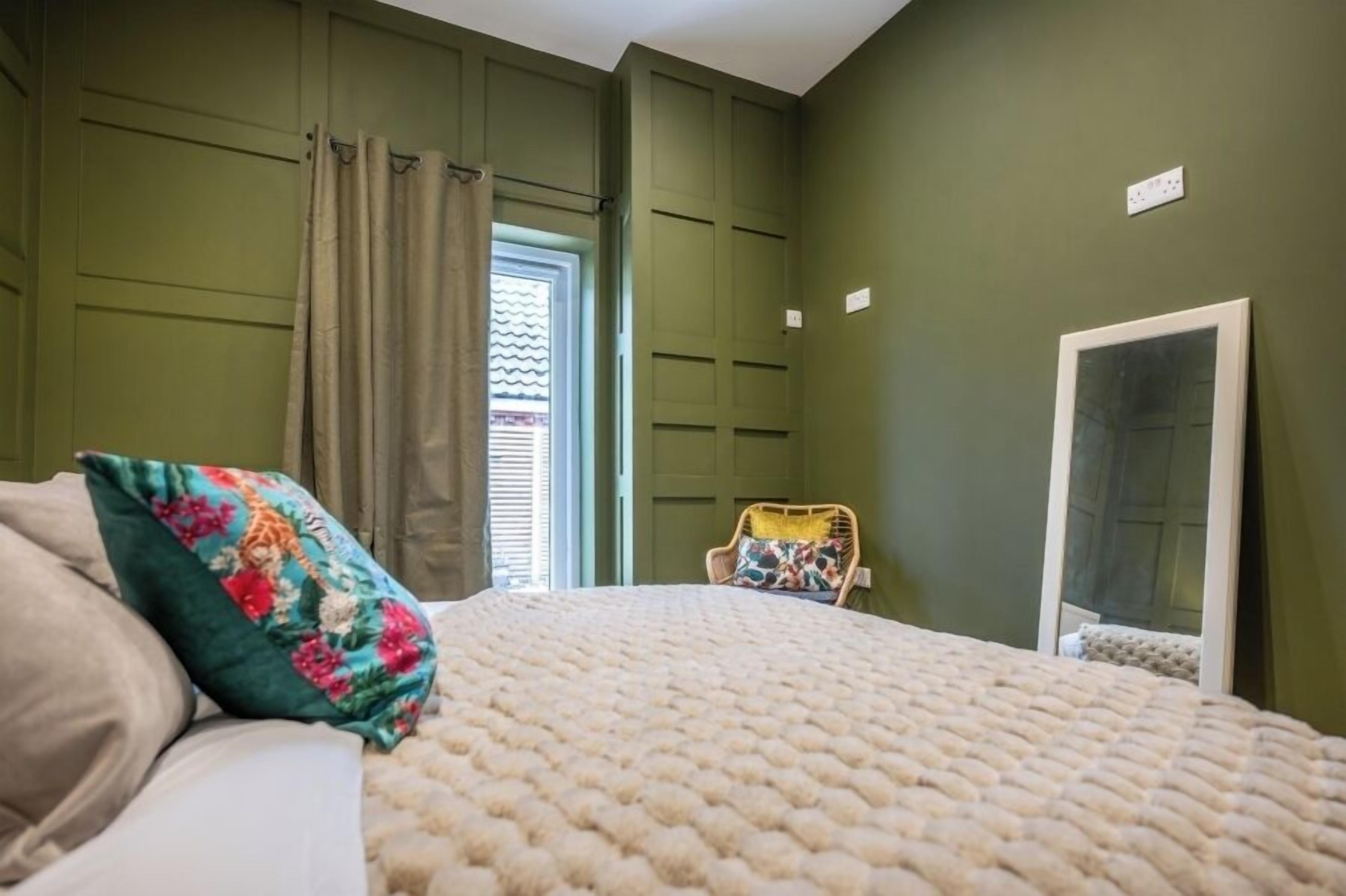 Quarto com cama, cadeira, janela com cortinas e porta.