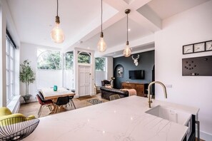Une cuisine moderne dotée d’un îlot en marbre, de luminaires suspendus et d’une grande fenêtre.