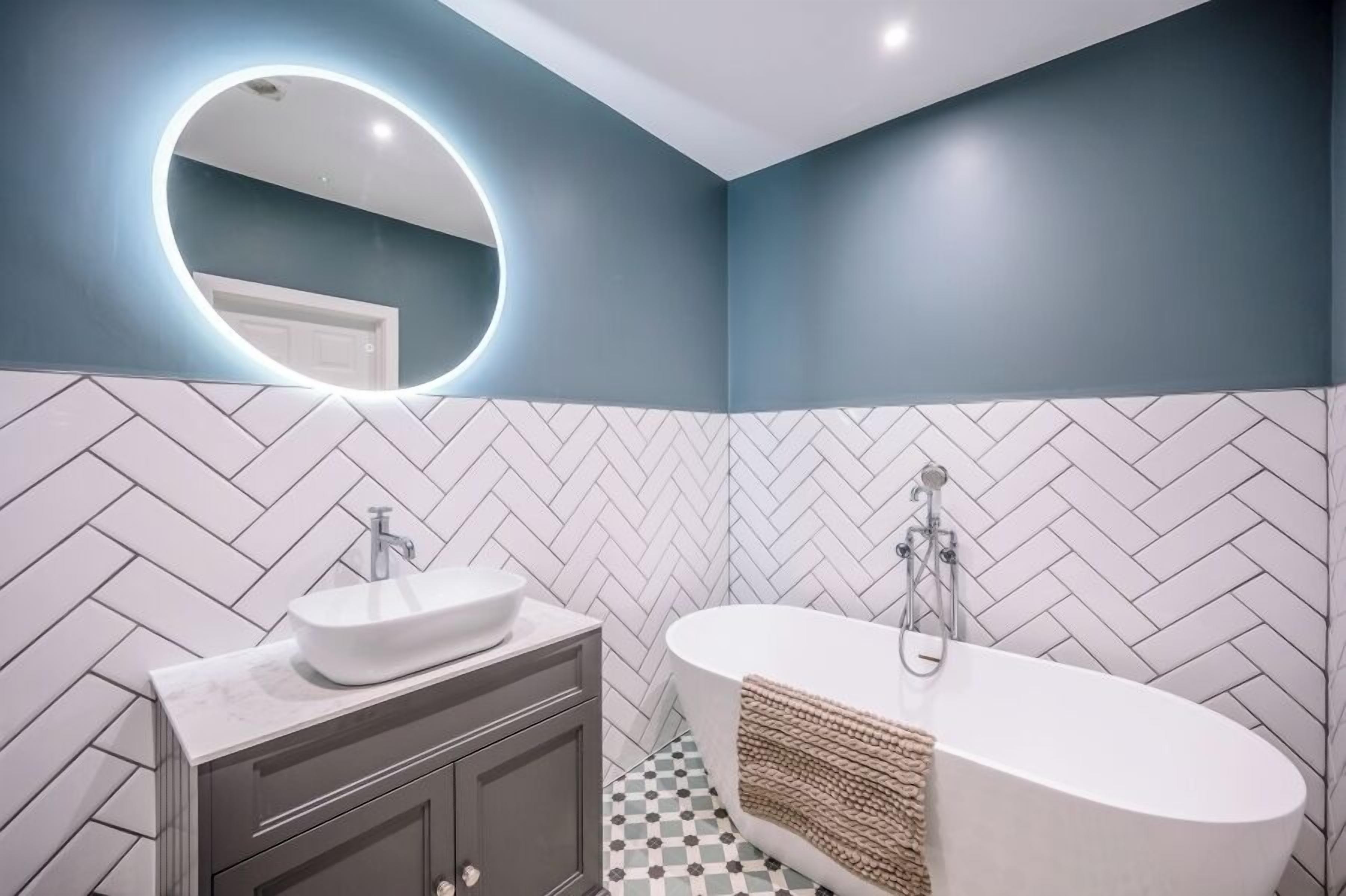 A modern bathroom with a herringbone tile pattern, a white sink, and a freestanding bathtub.