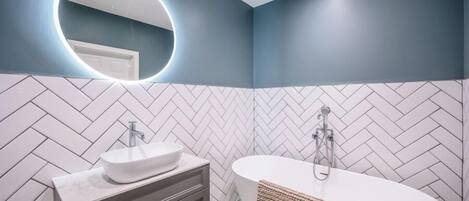 A modern bathroom with a herringbone tile pattern, a white sink, and a freestanding bathtub.