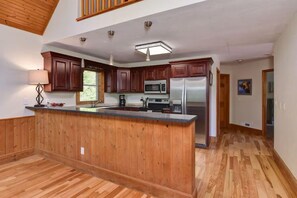 A spacious kitchen with wooden cabinets, a central island, stainless steel appliances, and a herringbone-patterned wooden floor. - Taylor Ranch Retreat | Hot Tub, Fire Pit & Ranch Views | Near Asheville (Fletcher)
