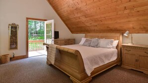 Ein Schlafzimmer mit Holzboden, einem Bett mit Kopfteil, einem Nachttisch, einer Kommode, einem Spiegel und einer Tür, die auf einen Balkon führt.