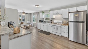Una cocina moderna con armarios blancos, electrodomésticos de acero inoxidable y una zona de comedor con mesa y sillas de madera.
