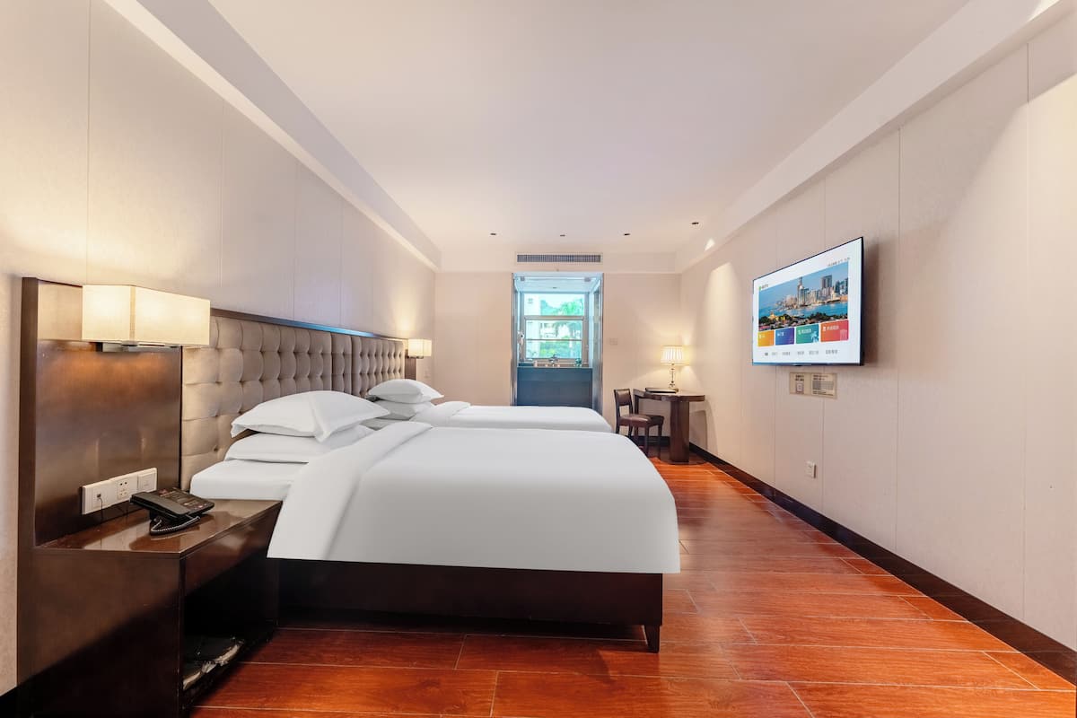 Una habitación de hotel con una cama grande, mesitas de noche, un escritorio y un televisor en la pared.