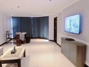 Un salon moderne avec un téléviseur à écran plat fixé au mur, un coin repas avec une table et des chaises, et une grande fenêtre ornée de rideaux bleus.