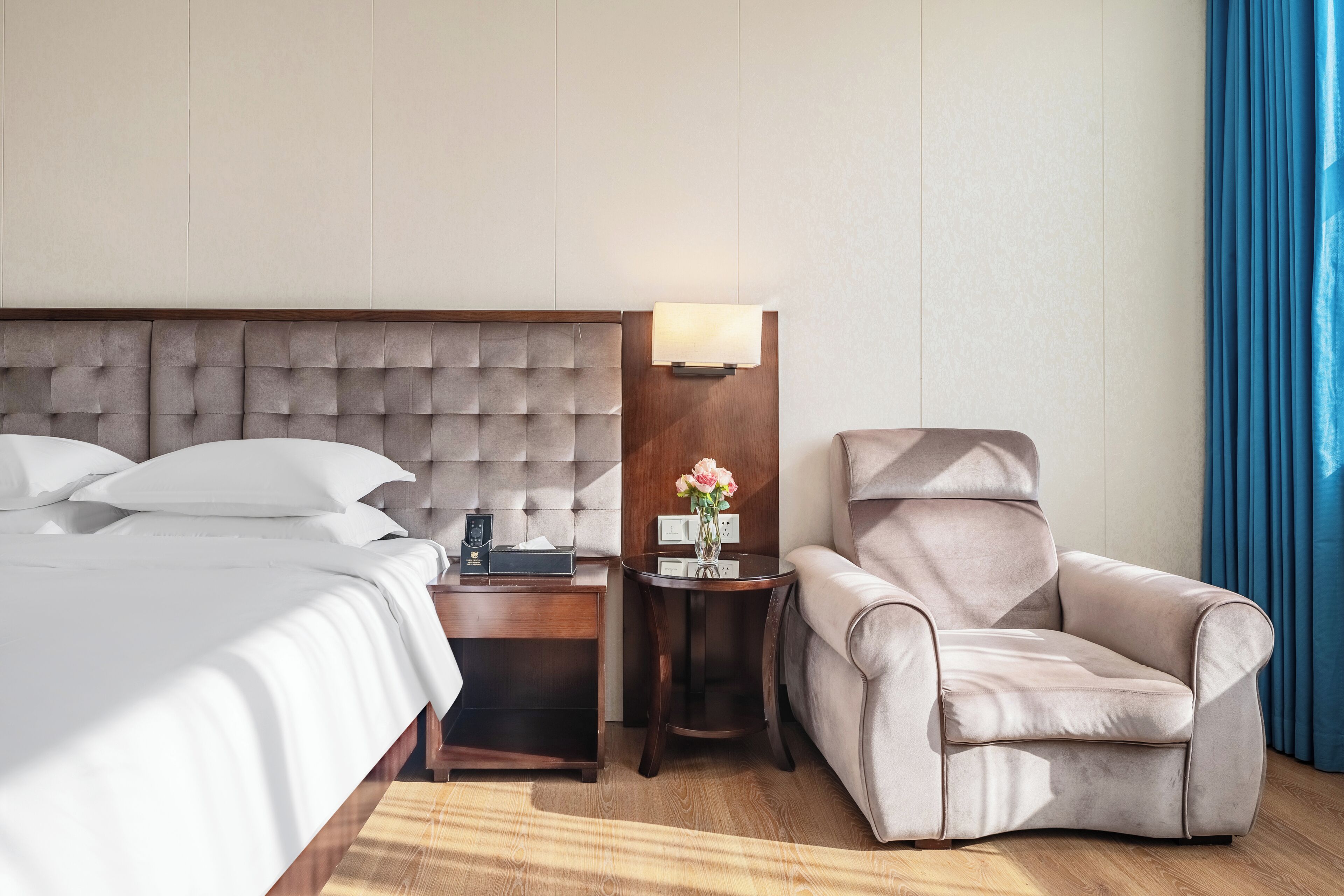 Habitación de hotel con una cama grande, una mesita de noche, una lámpara, una pequeña mesa con un florero y un sillón reclinable.