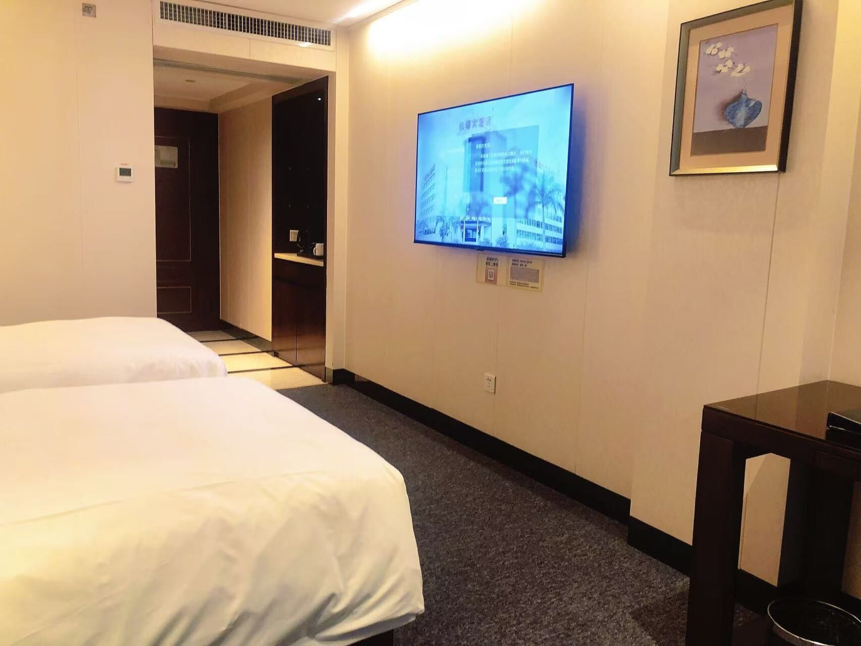 Una habitación de hotel con dos camas, un televisor montado en la pared y un cuadro enmarcado sobre el televisor.