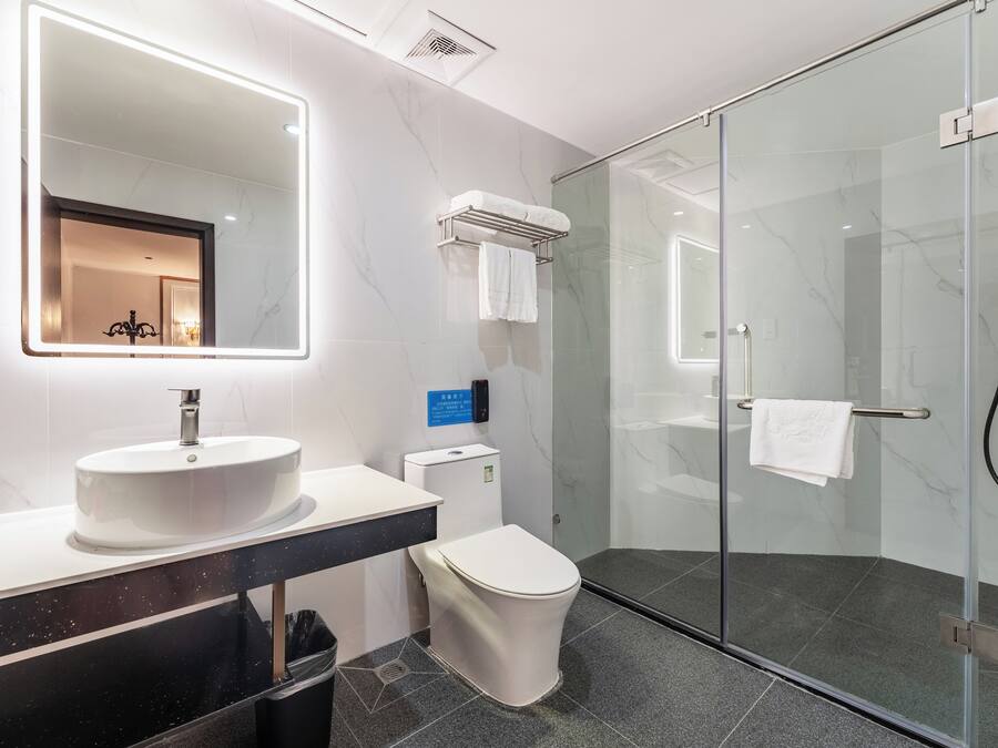 Un baño moderno con un espejo grande, lavabo blanco, inodoro y ducha con mampara de vidrio.