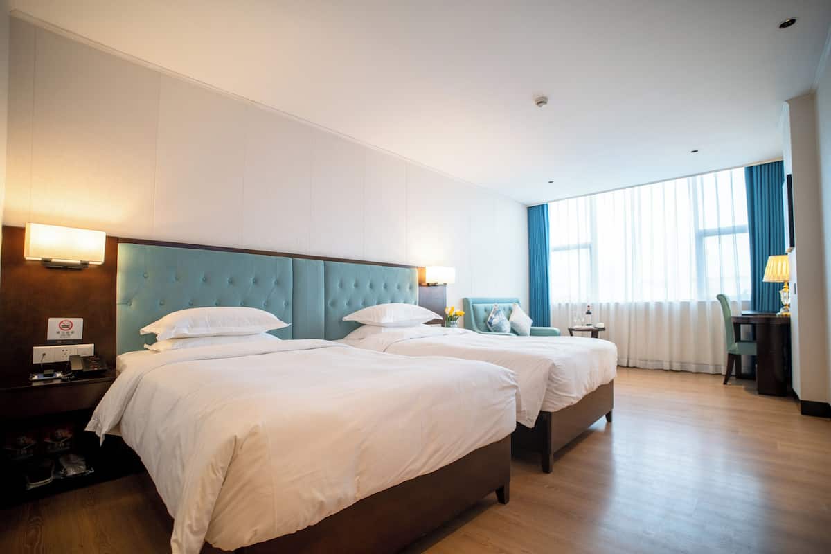 Habitación de hotel con dos camas, un escritorio y una ventana con cortinas.