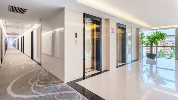 A modern hotel corridor with a polished floor, an elevator, and a potted plant by the window. - Shenzhen Airport Hotel Bao'an Airport  (Shenzhen)