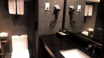 Un baño moderno con un lavabo negro, un inodoro y un espejo. Hay toallas colgadas en un perchero y un secador de pelo en la pared.