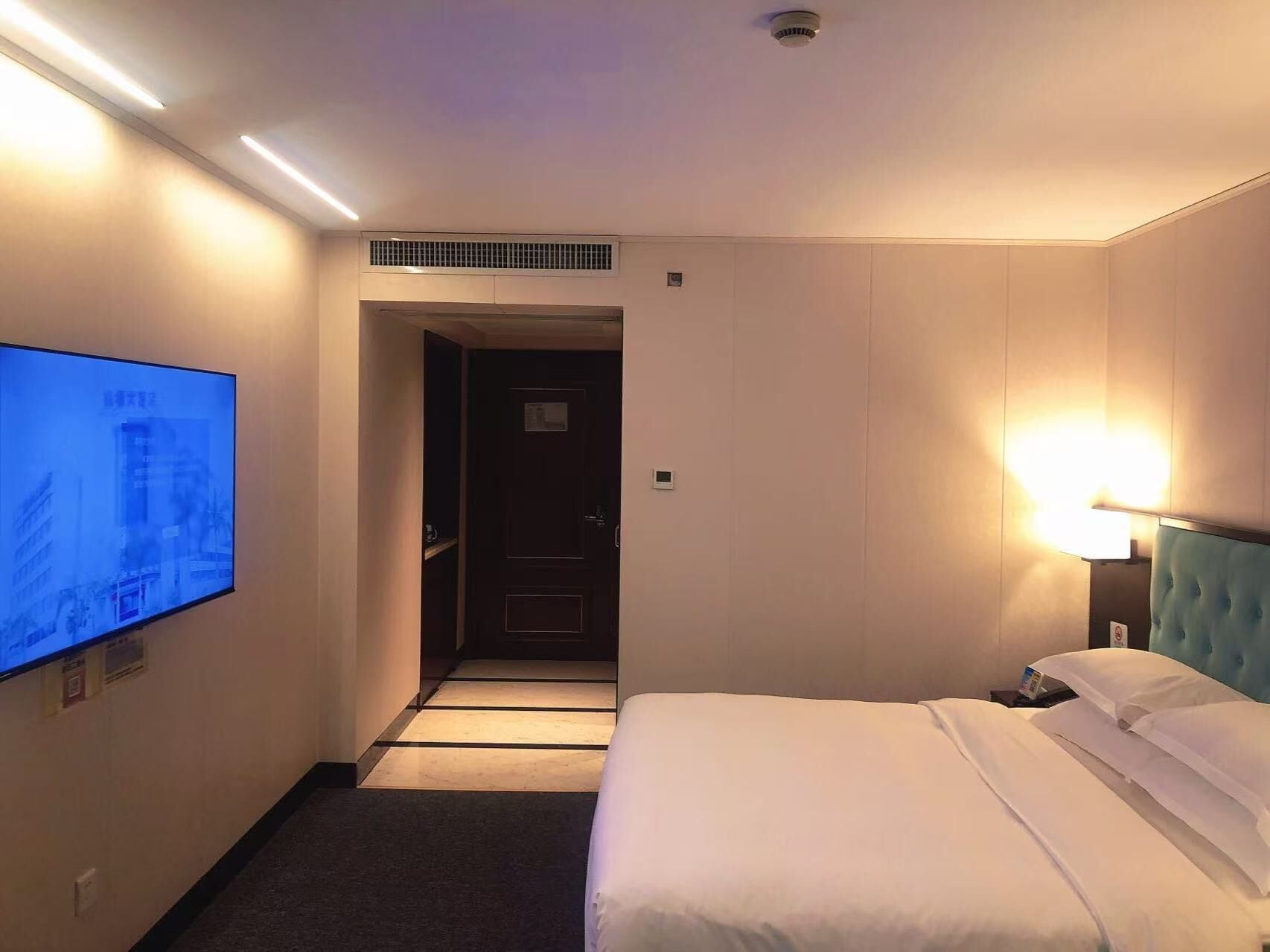 Una camera d'albergo con un letto, una TV a parete, una lampada da comodino e una porta che dà su un'altra stanza.