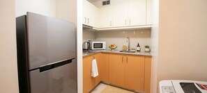 Een kleine keuken met een koelkast van roestvrij staal, een magnetron, een waterkoker en een spoelbak met een kraan.
