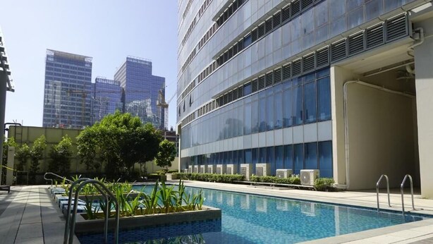 A modern building with a swimming pool, outdoor seating, and a view of other high-rise buildings. - Modern Central 1BR Apt - Prime City of BGC, Manila (Taguig)