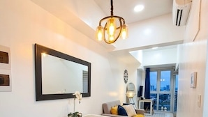 A modern living room with a dining area, a large mirror, a chandelier, and a view through a glass door. - Modern Central 1BR Apt - Prime City of BGC, Manila (Taguig)
