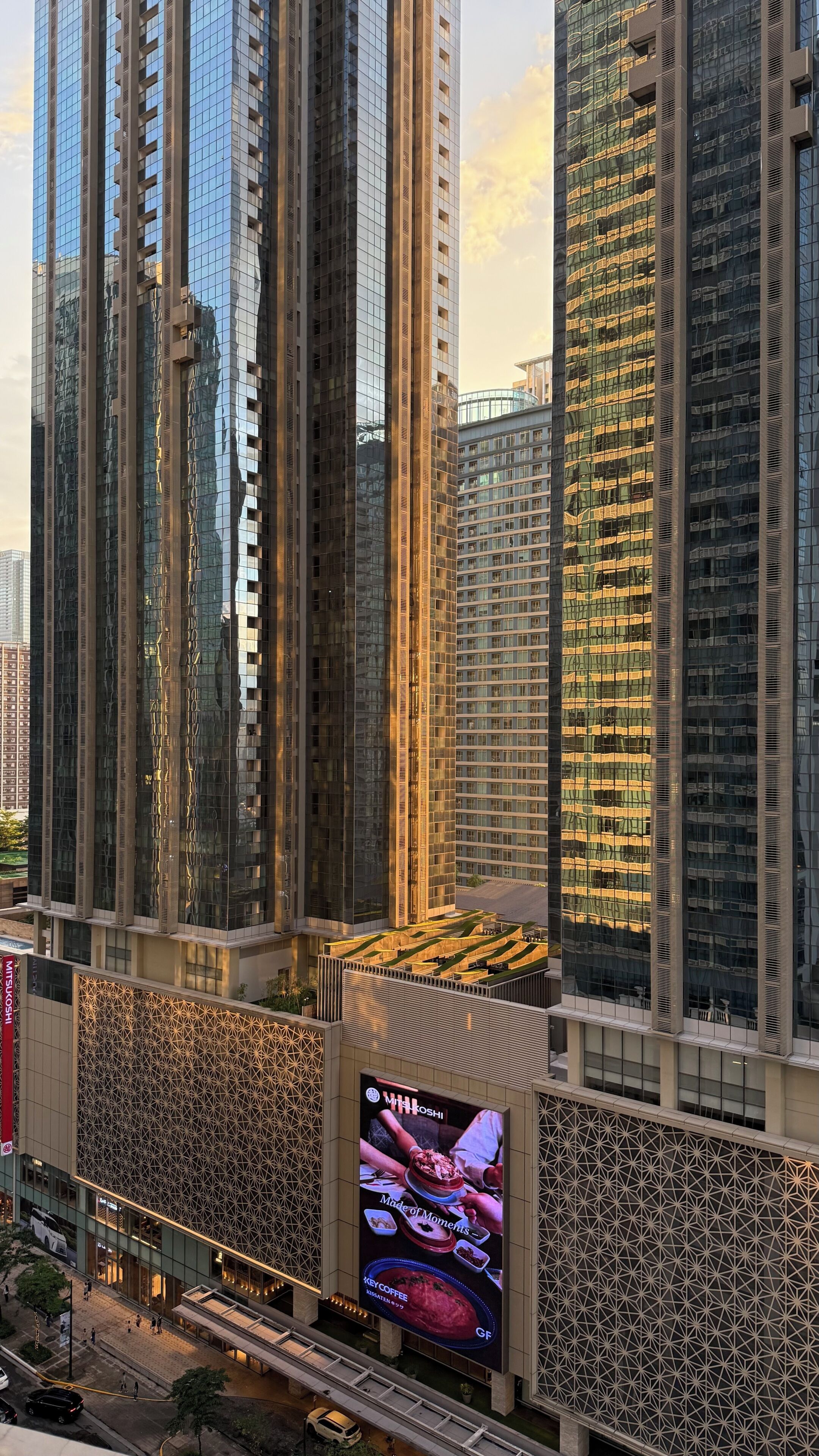 Um edifício alto com design arquitetônico moderno, fachadas de vidro refletivas e um painel digital de destaque publicando um restaurante.