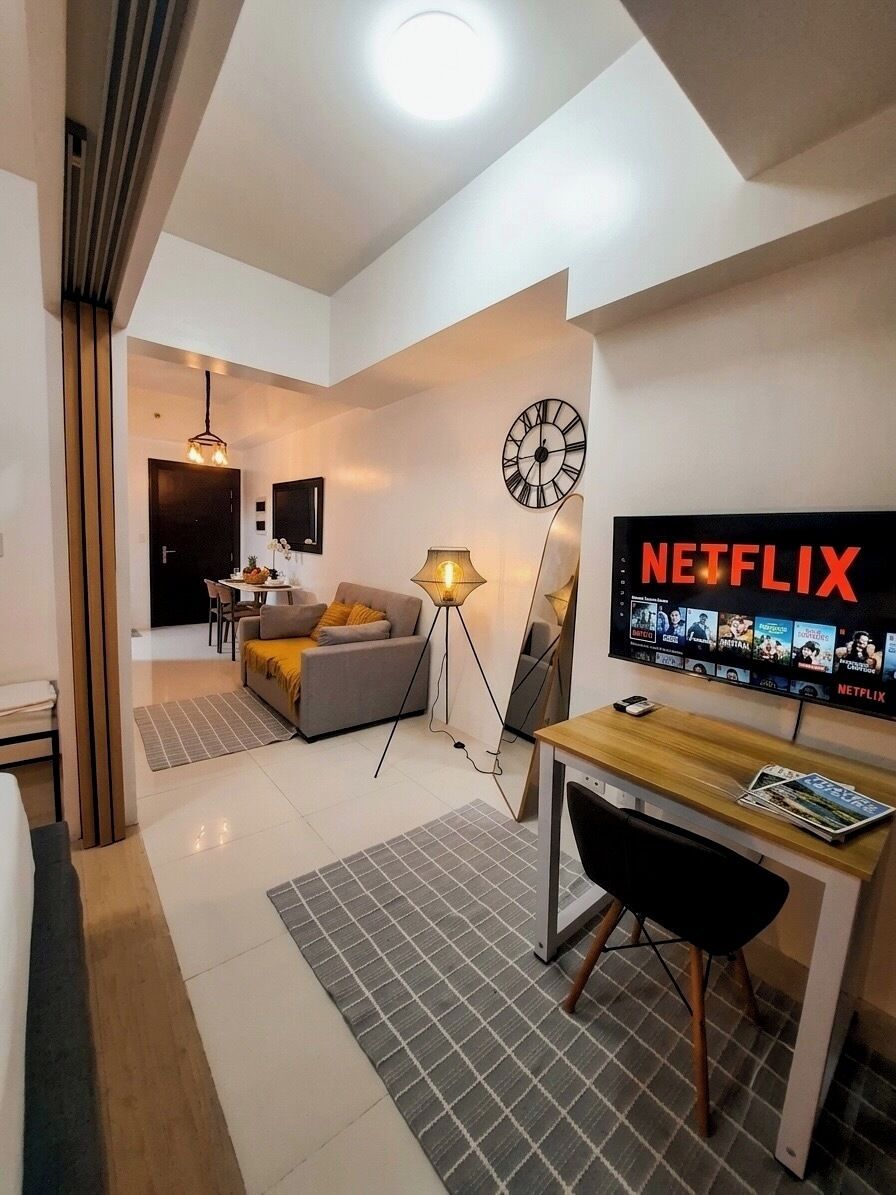 A modern living room with a flat-screen TV displaying Netflix, a sofa, a coffee table, and a dining area with chairs.