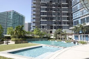 A modern building complex with a central swimming pool surrounded by greenery and palm trees. - Modern Central 1BR Apt - Prime City of BGC, Manila (Taguig)