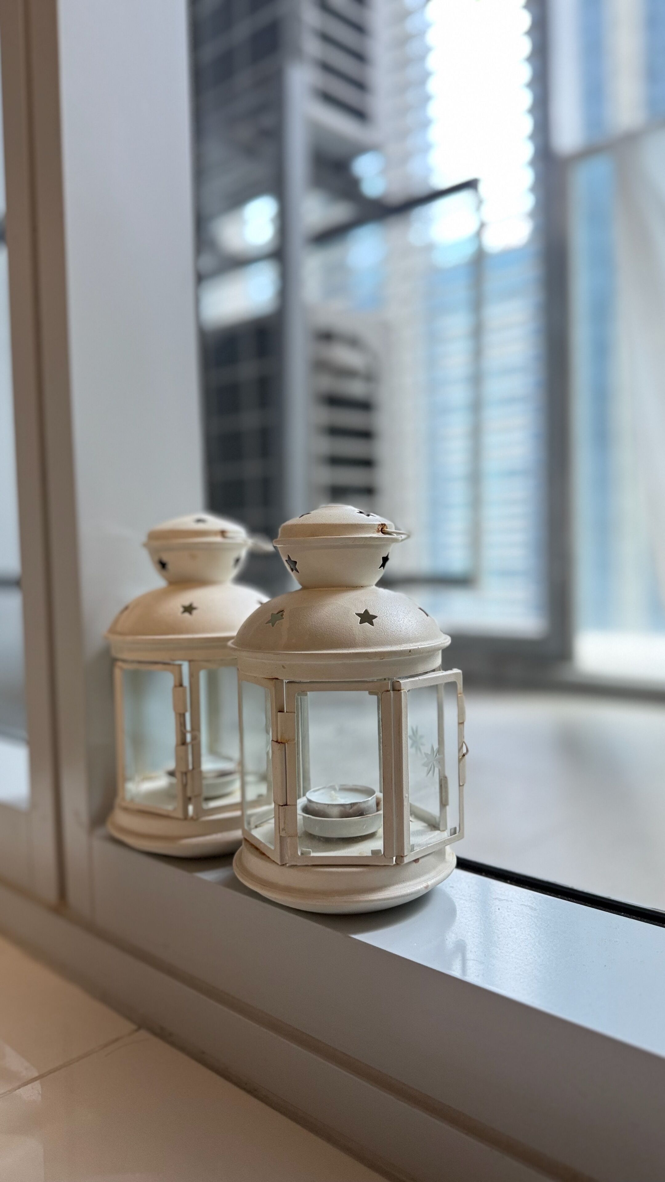 Twee witte lantaarns met stersieraden op een vensterbank.