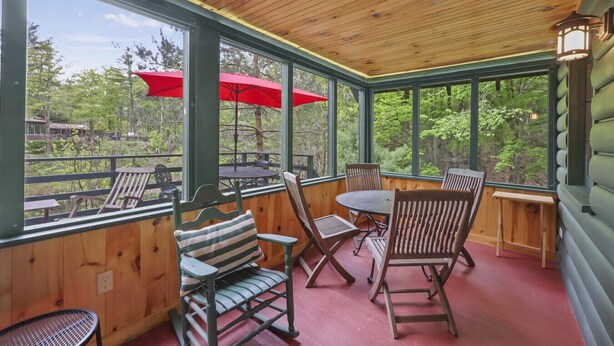 A covered outdoor seating area with wooden furniture and large windows.