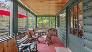 A covered porch with wooden chairs, a table, and a red umbrella.