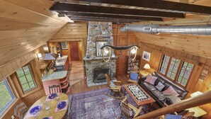A cozy cabin interior with a stone fireplace, wooden walls, a dining area, and a living room with a sofa and chairs.