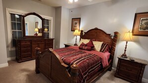 Une chambre à coucher avec un lit en bois, un ventilateur de plafond, une commode, un miroir et deux tables de chevet avec des lampes.