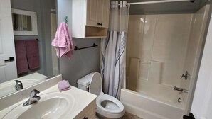 Une salle de bain équipée d’un lavabo, de toilettes et d’une baignoire. Un miroir est placé au-dessus du lavabo, et un porte-serviettes contient des serviettes.