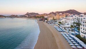 Un hôtel situé sur la côte, avec accès direct à la plage, composé de plusieurs bâtiments et offrant une vue sur les montagnes.