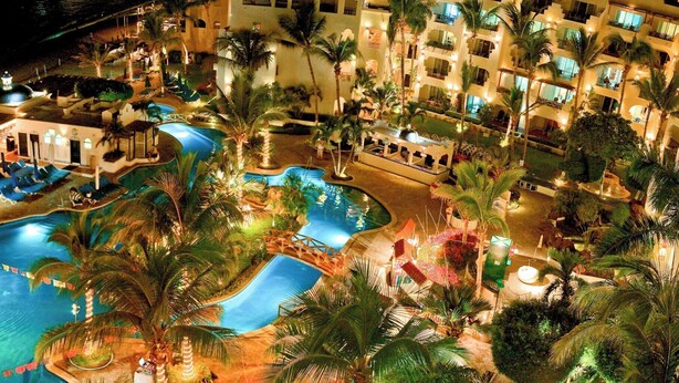 Un complexe hôtelier doté de plusieurs piscines, de palmiers et d’un immeuble à étages avec des balcons.