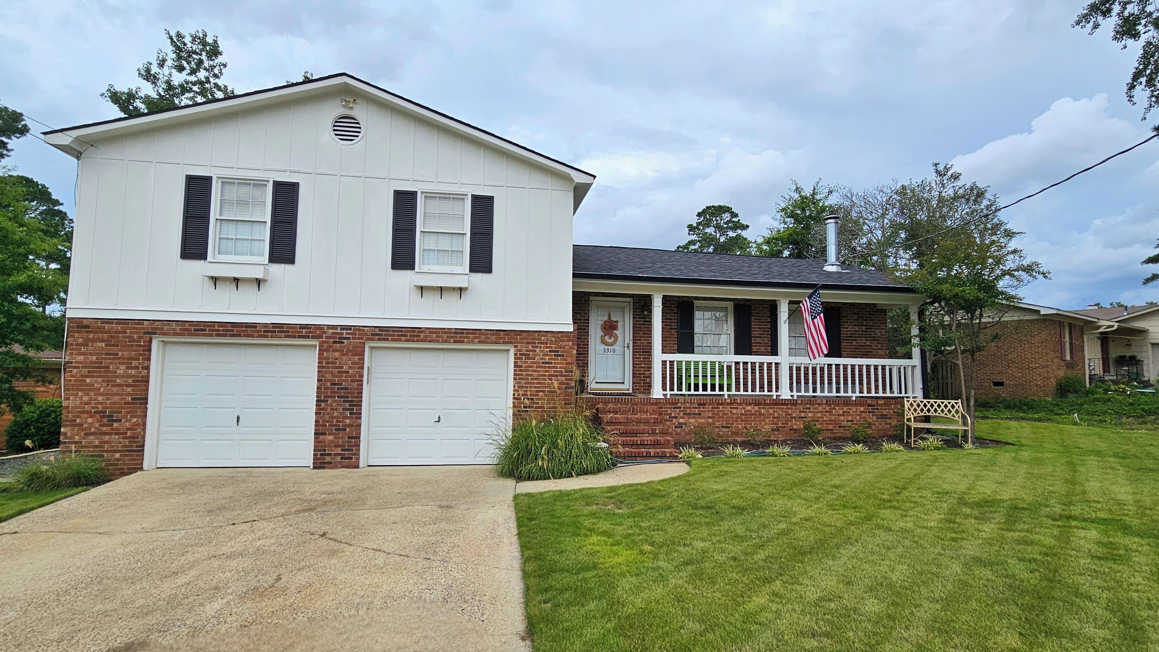 A two-story house with a garage, a porch with a railing, and an American flag.