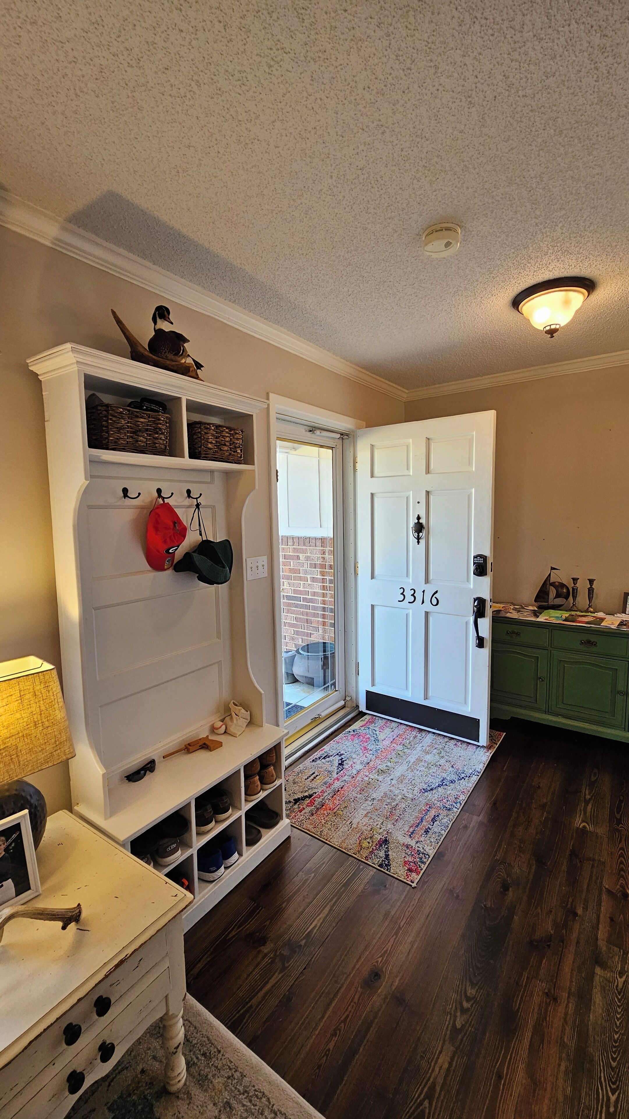 A hallway with a white door marked 3316, a shoe rack, and a small table with a lamp.