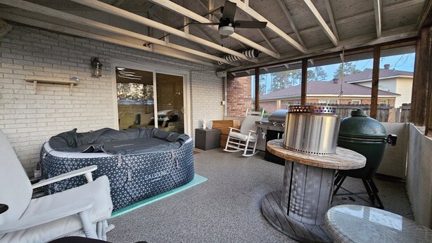 Een overdekt terras met een jacuzzi, een barbecue en een schommelstoel.