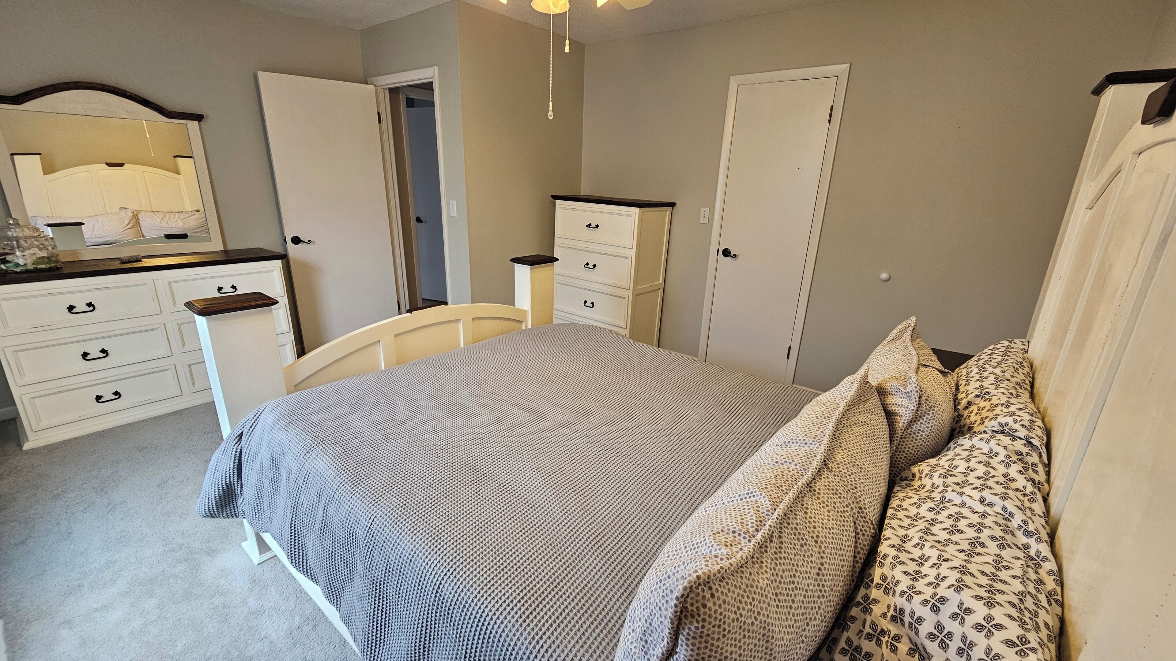 Een slaapkamer met een bed, een dressoir, een kledingkast en een spiegel.