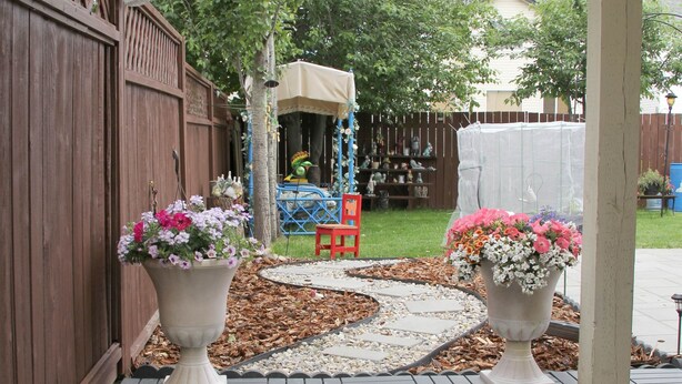 Un'area patio con due grandi vasi di fiori, una recinzione in legno e una struttura giochi sullo sfondo.