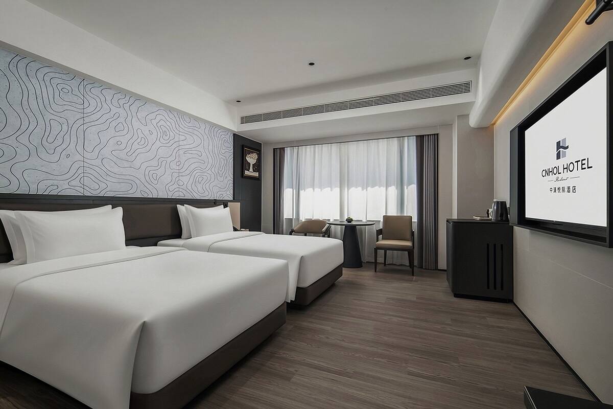 Une chambre d’hôtel avec deux lits, un bureau, une chaise et une grande fenêtre avec des rideaux.